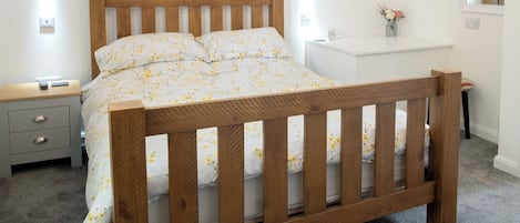 A bedroom with a wooden bed, a bedside table, a nightstand, a small desk, and a mirror on the wall.