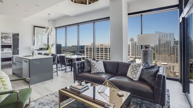 A modern living room with a leather sofa, a coffee table, and a city view through large windows. - La Brise by Atlanta Luxury Rentals (Atlanta)