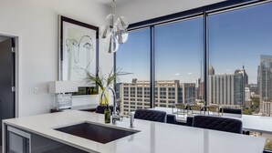 A modern kitchen with a large island, a dining area with dark upholstered chairs, a large window with a city view, and a framed abstract painting on the wall. - La Brise by Atlanta Luxury Rentals (Atlanta)