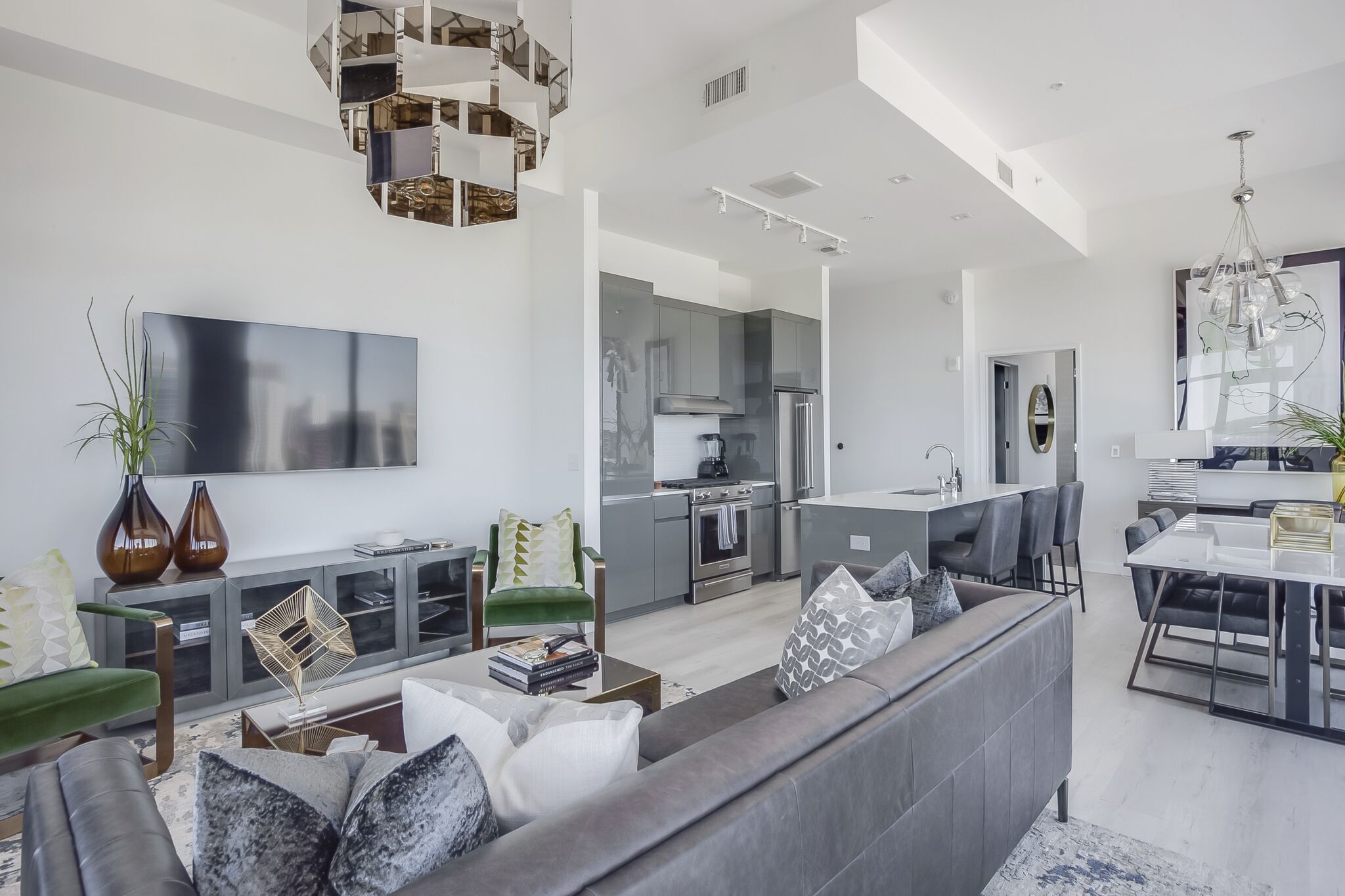 Un salon moderne avec un canapé gris, un téléviseur à écran plat et un coin repas comprenant une table et des chaises blanches.
