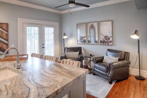 A modern kitchen with a marble countertop, a ceiling fan, and a dining area with leather chairs.