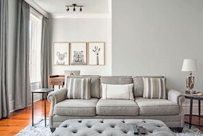 A living room with a grey sofa, a small table, a lamp, and framed pictures on the wall.