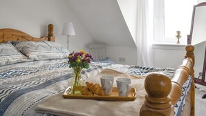 A neatly made bed with patterned bedding, a bedside table with a tray of croissants, a vase with flowers, and a bedside lamp. - 2 bedroom accommodation in Collieston, near Ellon (Collieston, near Ellon)