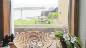 A view through a window of a coastal area with a boat, a grassy lawn, and a building. - 2 bedroom accommodation in Collieston, near Ellon (Collieston, near Ellon)