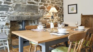 A dining area with a stone wall, a wooden table set for two, and a table lamp. - 2 bedroom accommodation in Collieston, near Ellon (Collieston, near Ellon)