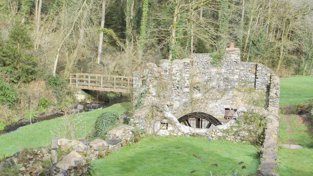Una estructura de piedra con un puente de madera, un pozo de piedra y una zona con césped.