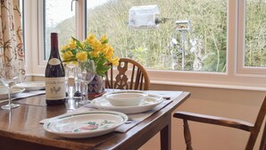 Una mesa de comedor dispuesta con platos, una botella de vino y un florero con flores amarillas.