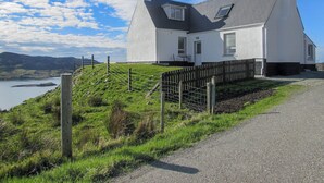 Una casa blanca amb teulada gris, pati tancat per una tanca i un cos d'aigua al fons.
