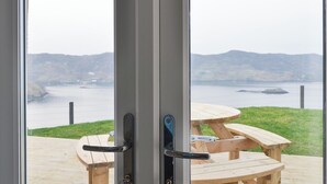 Vista a través d'una porta de vidre, amb taula de picnic de fusta i barana metàl·lica.
