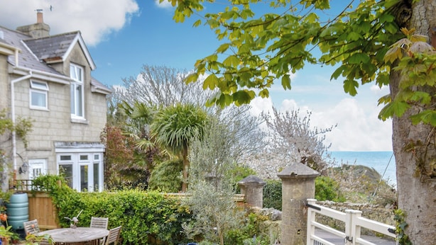 A garden with a stone wall, a white gate, and a cobblestone patio. - 3 bedroom accommodation in St Lawrence (St Lawrence)