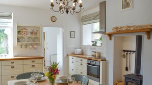 A dining area with a wooden table set for six, surrounded by chairs. A chandelier hangs from the ceiling, and a clock is visible on the wall. - 3 bedroom accommodation in St Lawrence (St Lawrence)