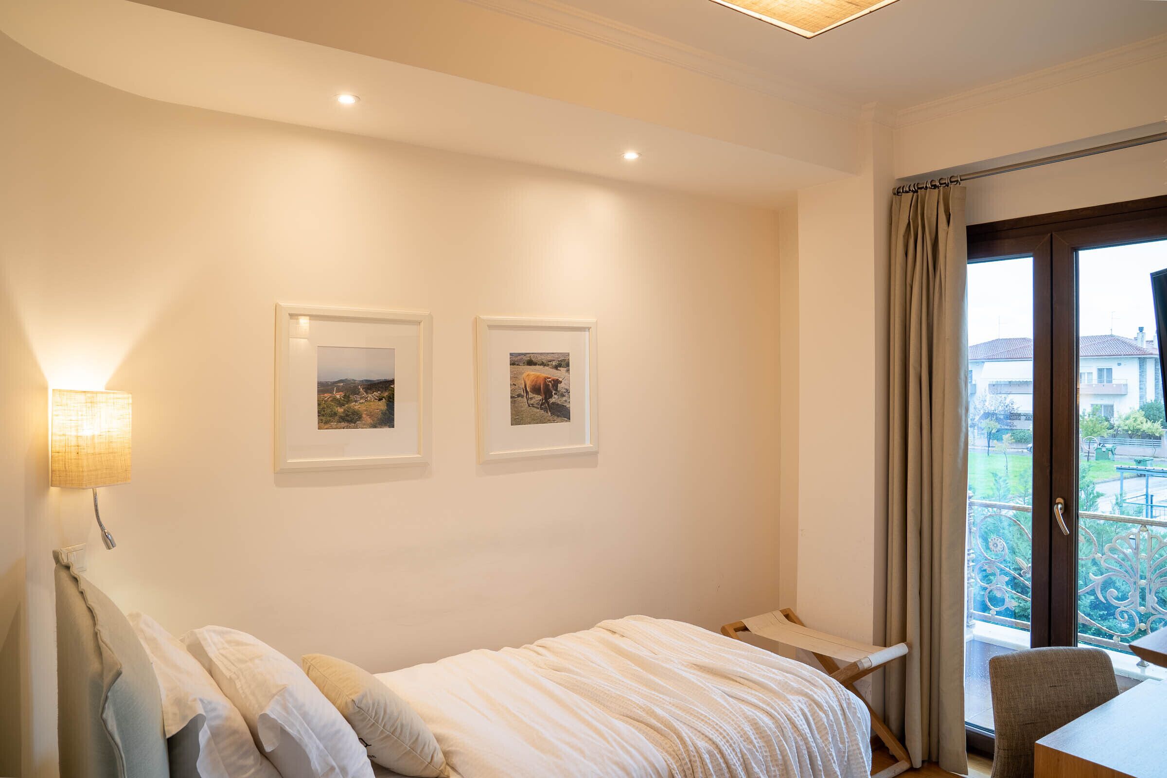 A bedroom with a bed, a desk, and a balcony with a railing.