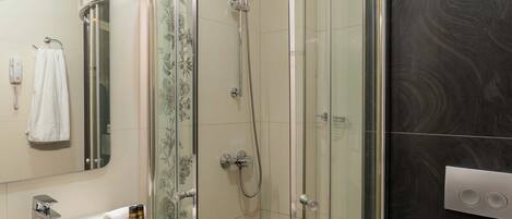 Un baño moderno con ducha envuelta en cristal, un lavamanos blanco con encimera de madera y un espejo sobre el lavamanos.