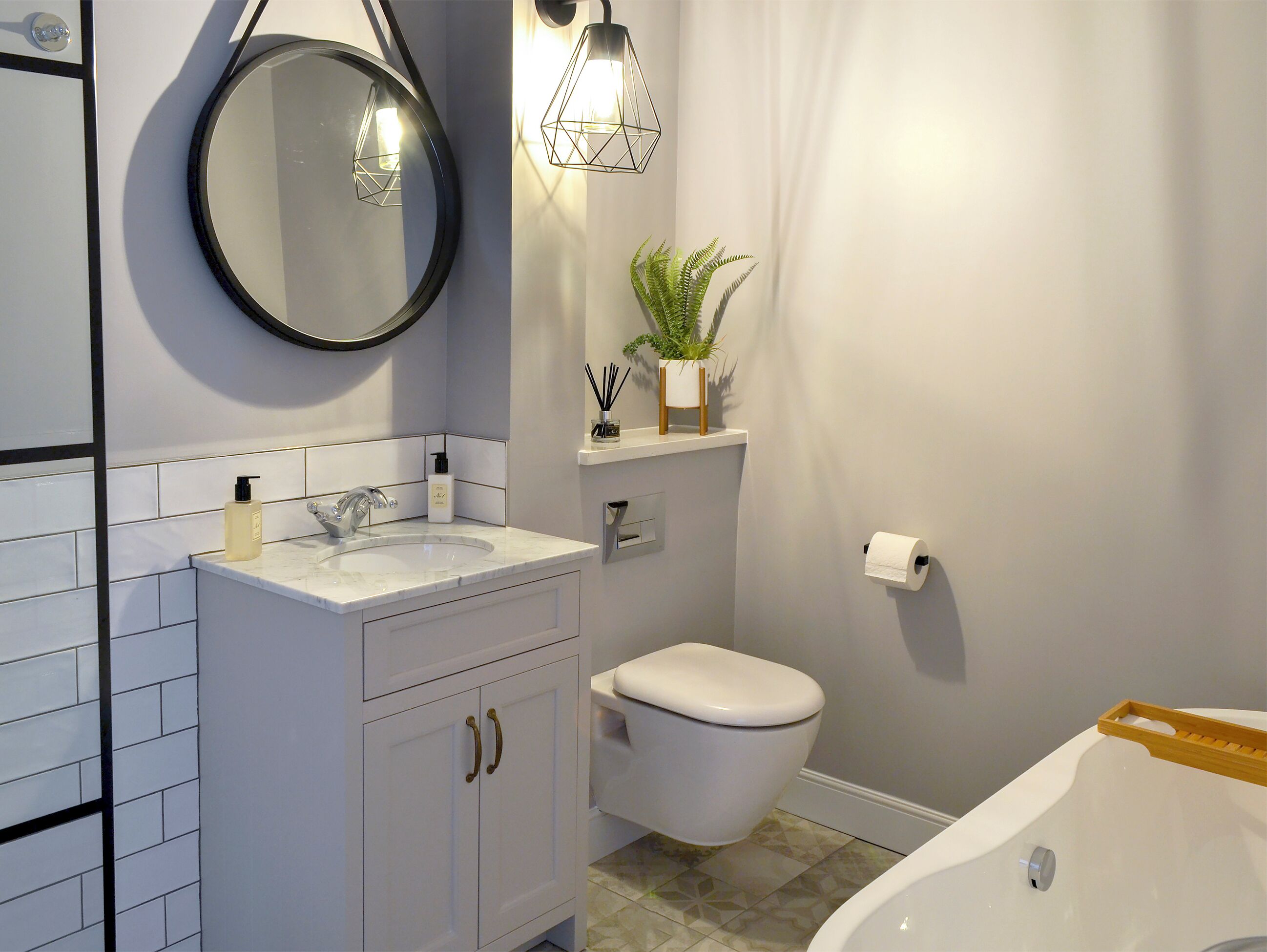 Een badkamer met een wit wastafel, spiegel en toilet. Er staat een plant aan de muur en een plank met toiletartikelen.