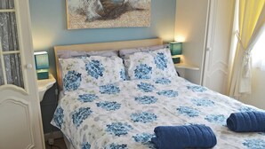 Un dormitorio con cama, dos mesitas de noche, un tocador, un cuadro en la pared y una ventana con cortinas.