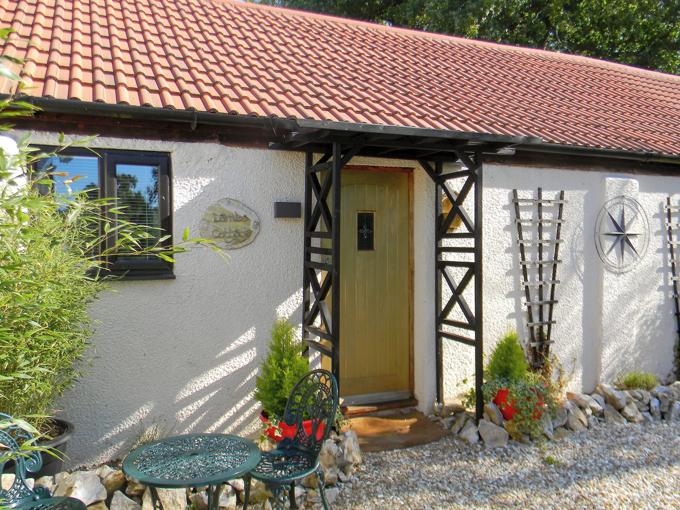 A cottage with a tiled roof, a door, and a small garden with a table and chairs.