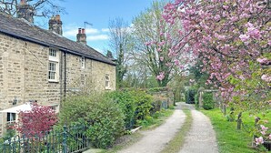 A stone building with a gravel driveway, surrounded by greenery and flowering trees. - 2 bedroom accommodation in Bewerley, near Pateley Bridge (Bewerley, near Pateley Bridge)