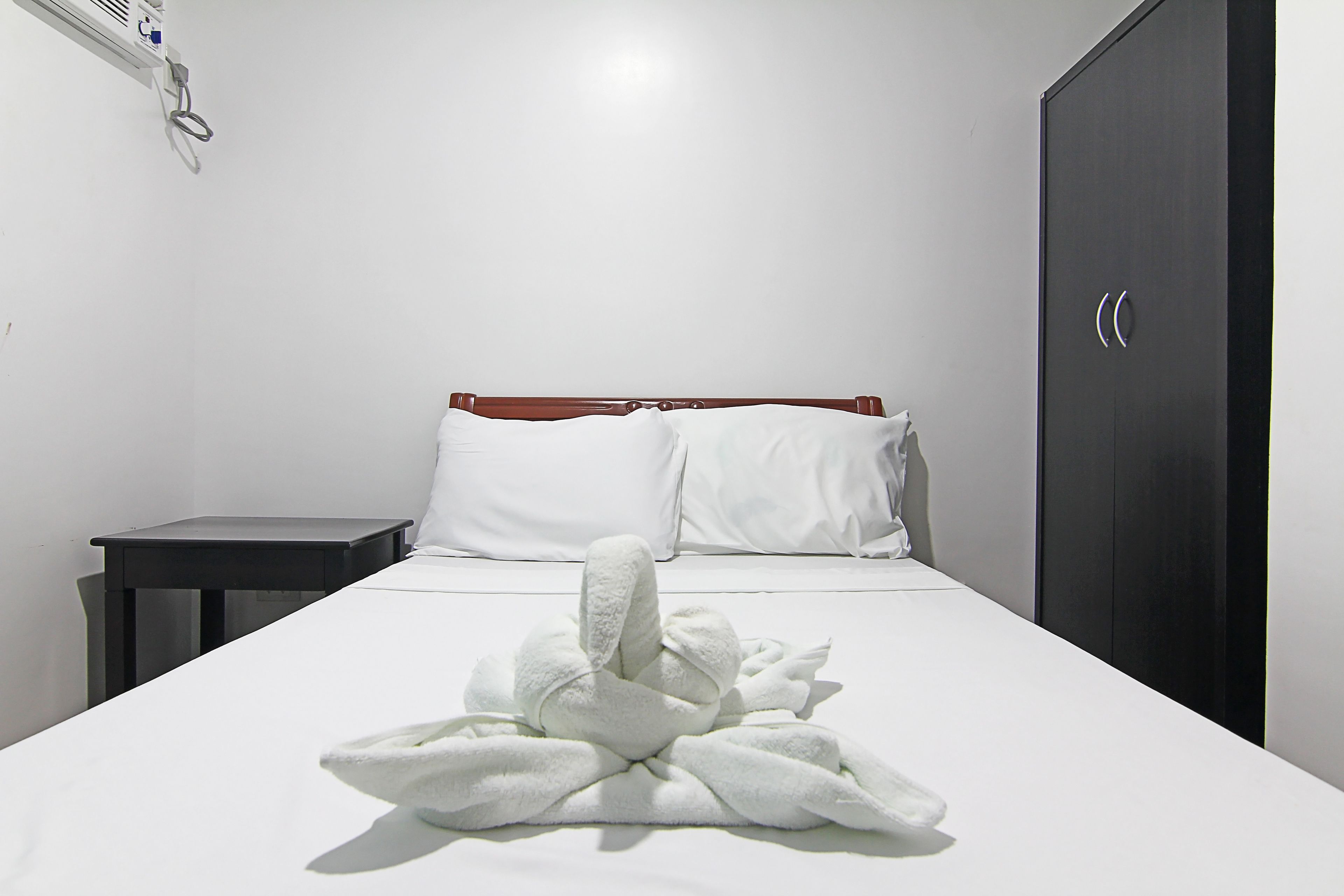 A hotel room with a neatly made bed, a small bedside table, and a wardrobe.