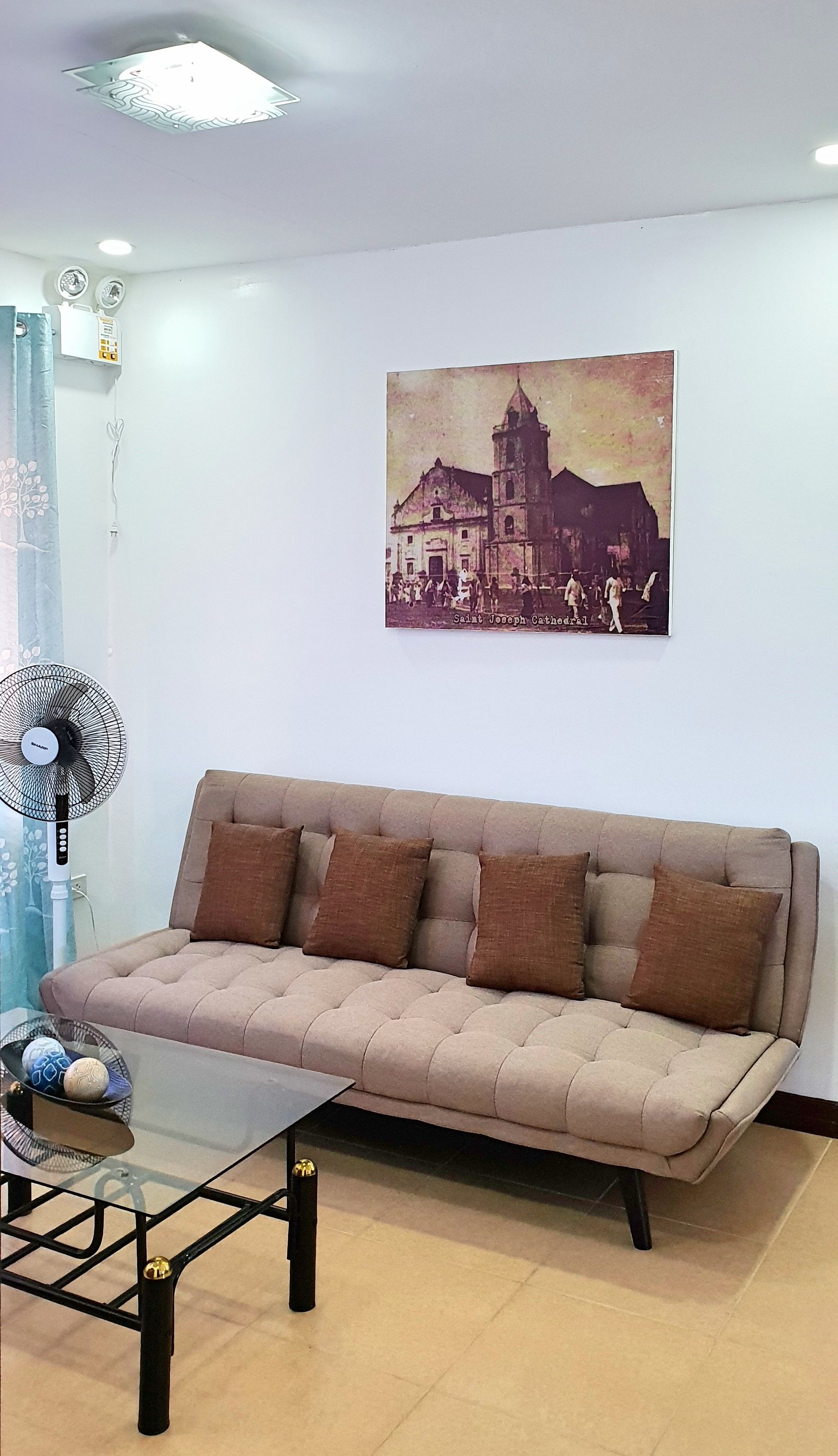 Un salon avec un canapé beige, une table basse en verre et un tableau représentant la cathédrale Saint-Joseph, accroché au mur.