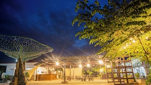 An outdoor seating area with tables and chairs, a decorative tree structure, and a building in the background.
