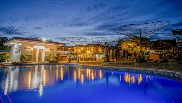 A swimming pool with a reflection of lights, surrounded by a building with a covered outdoor area and a gazebo.