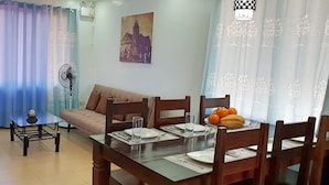 A dining area with a table set for four, a sofa, and a fan.