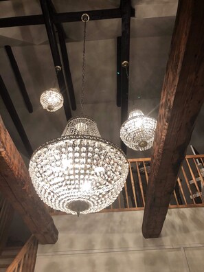A chandelier with multiple crystal elements hanging from a ceiling with exposed wooden beams. - Døstrup Landevejskro & Motel (Skaerbaek)
