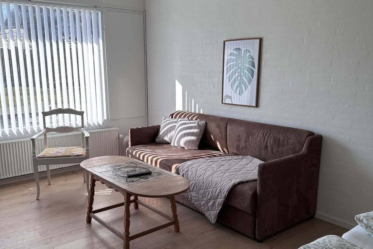 A modern living room with a brown sofa, a wooden coffee table, a patterned blanket, and a framed artwork on the wall.