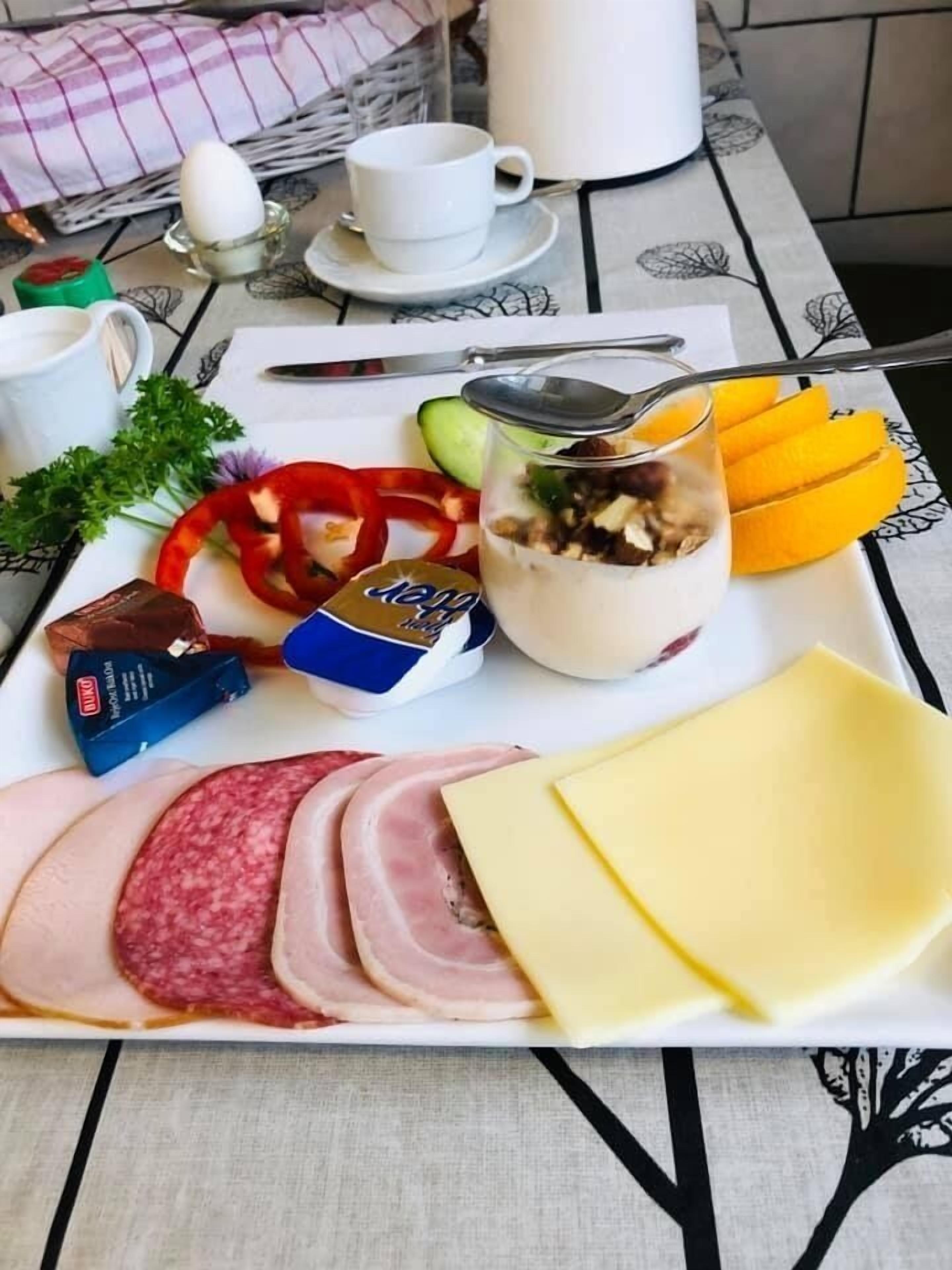 A breakfast tray with ham, cheese, sliced fruits, a yogurt parfait, and condiments.