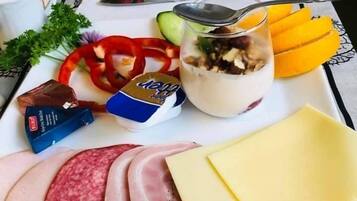 A breakfast tray with ham, cheese, sliced fruits, a yogurt parfait, and condiments.