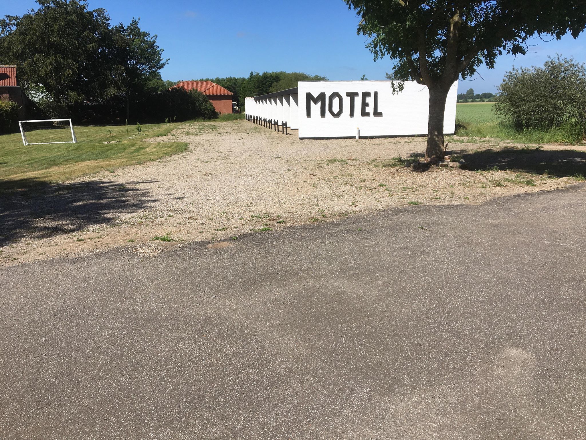 A motel sign with a gravel path leading to it, surrounded by greenery and a clear sky.