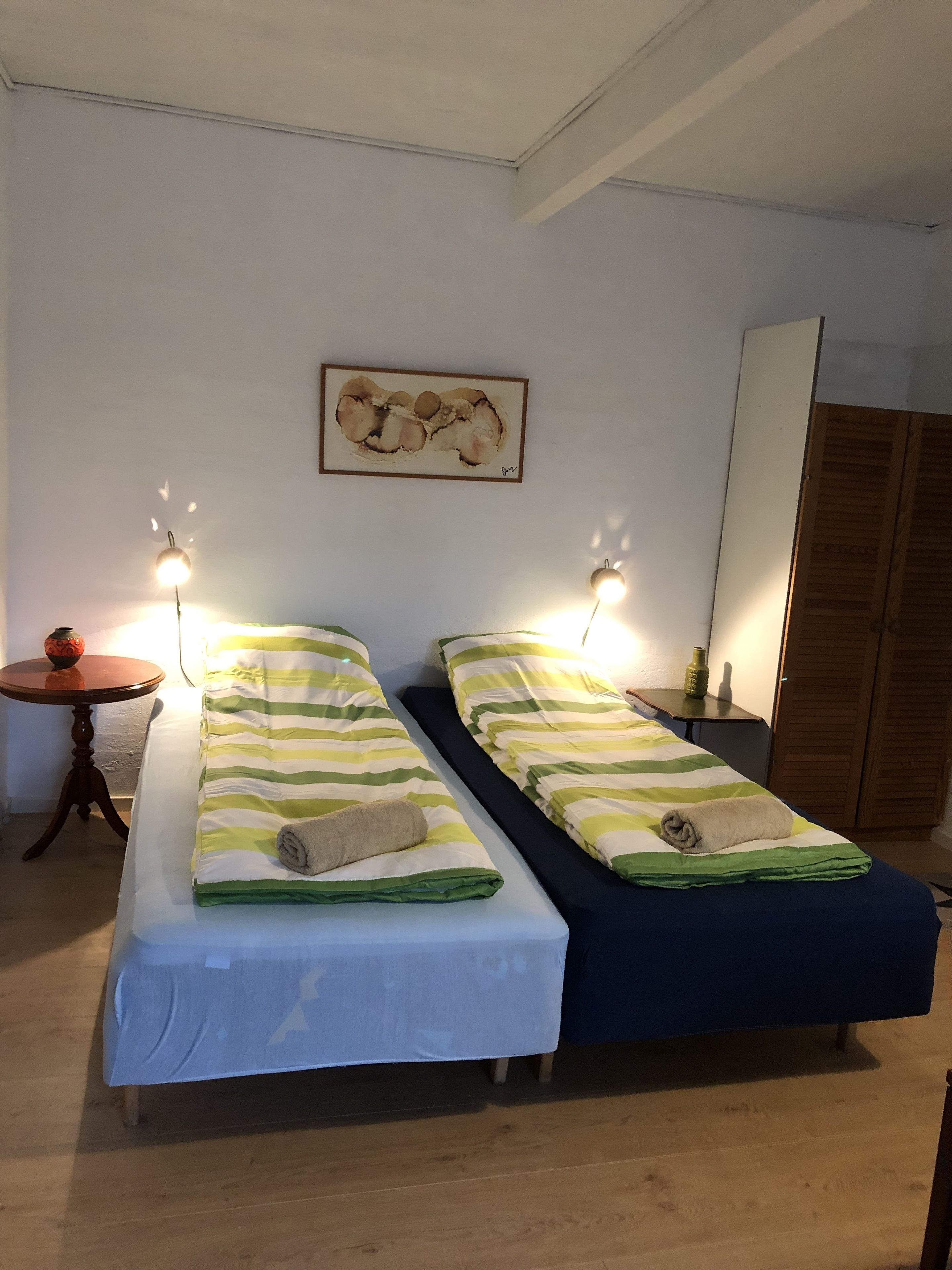 Ein Zimmer mit zwei Einzelbetten, einem kleinen runden Tisch, einem Wandbild und einem Holzschrank.