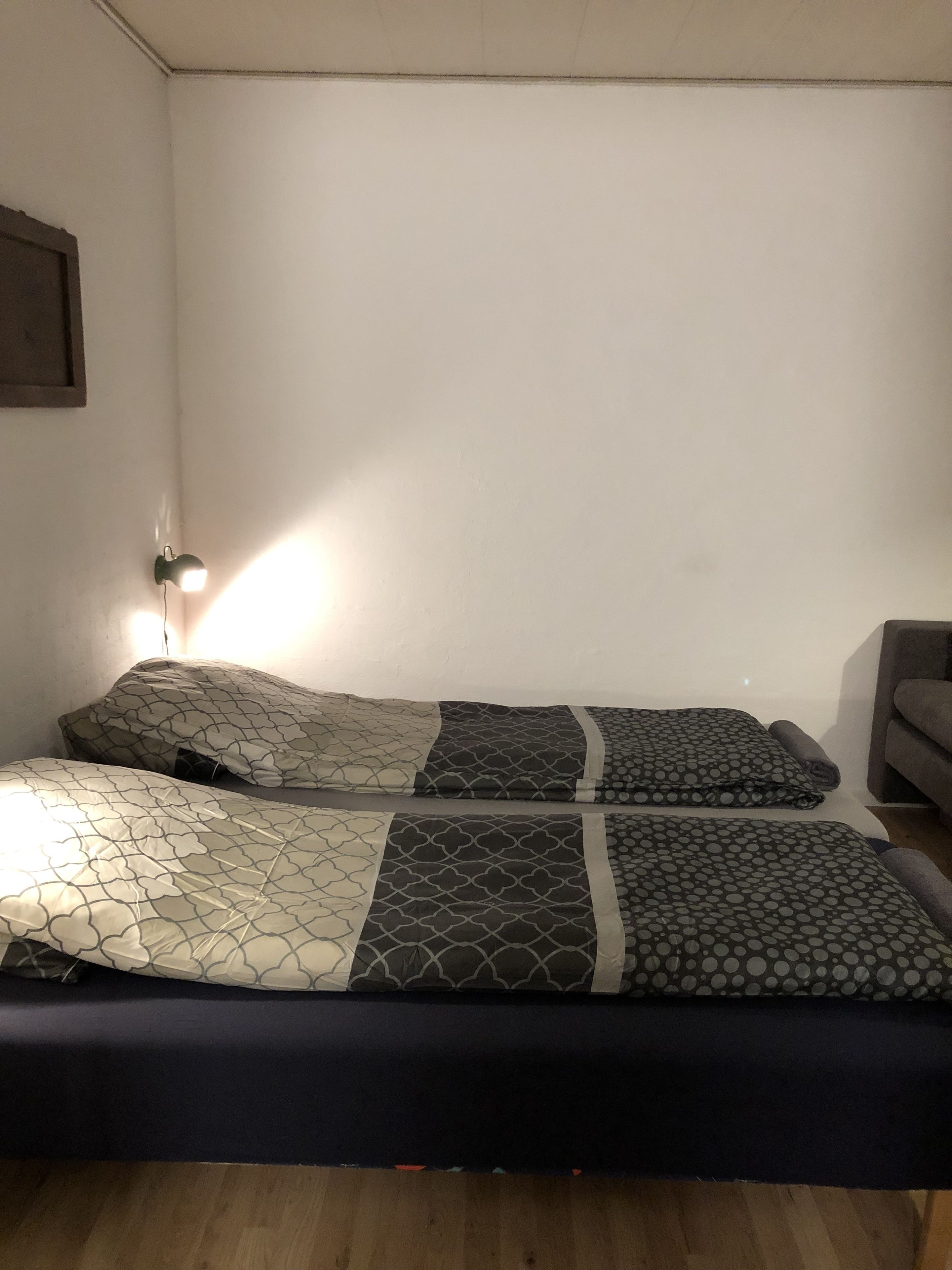 Et værelse med to senge, et natbord, en lampe og trægulv.