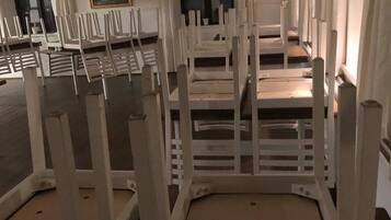 Una habitación con varias sillas blancas dispuestas en filas, un cuadro en la pared y una ventana con cortinas.