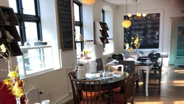 A dining area with a round table, chairs, and a vase with flowers. There are windows with black frames and a chalkboard on the wall. - Døstrup Landevejskro & Motel (Skaerbaek)