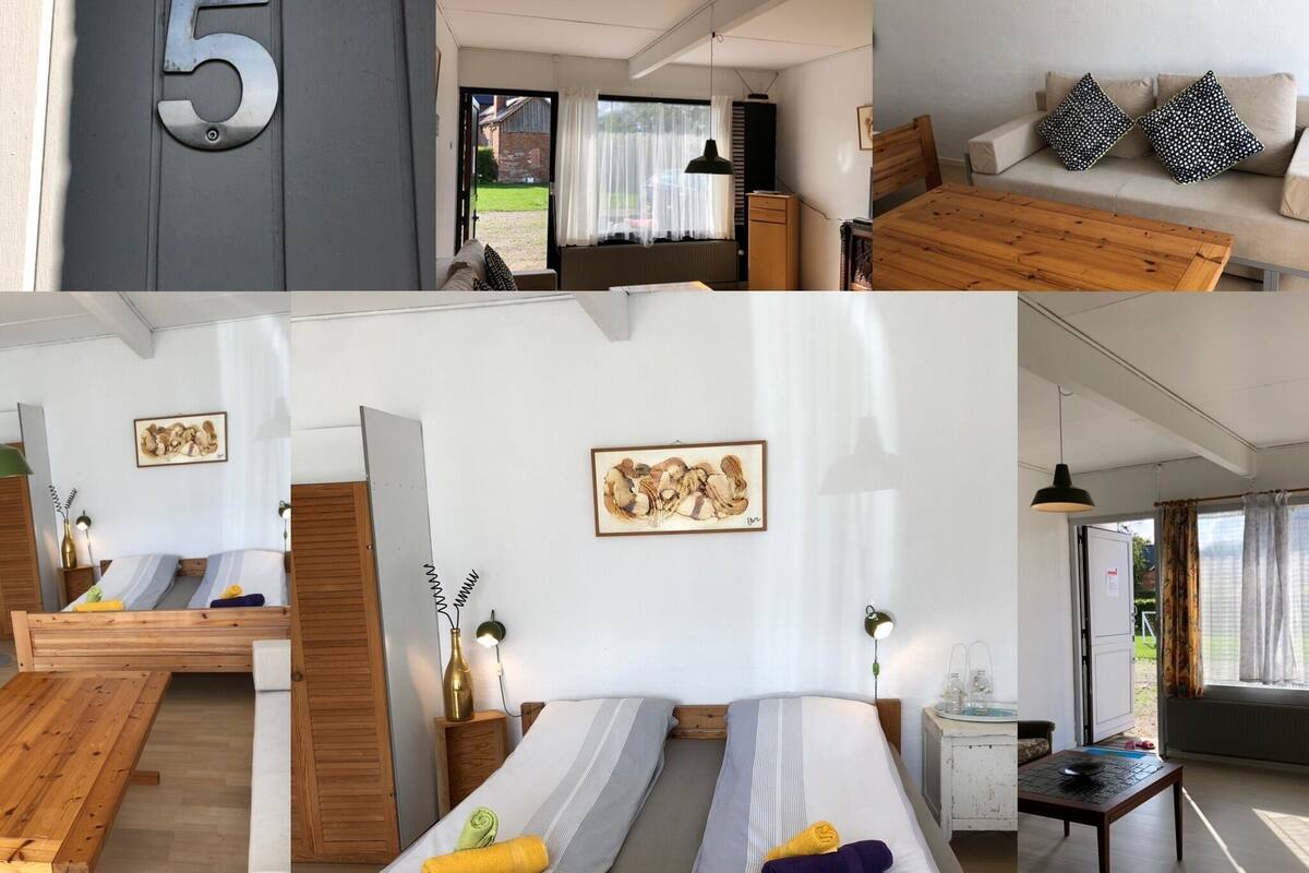 A modern room with a bed, a wooden table, a sofa, and a bathroom with a sink and toilet.