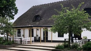 A building with a thatched roof, a covered outdoor seating area with tables and chairs, and a well-maintained lawn. - Døstrup Landevejskro & Motel (Skaerbaek)