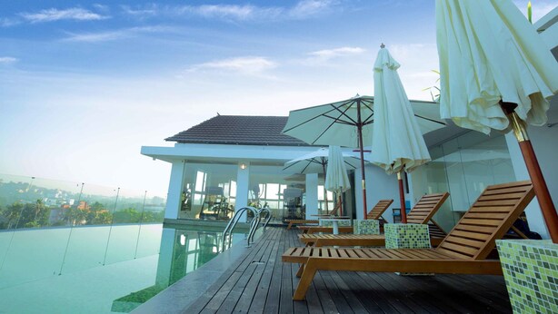 A poolside area with lounge chairs and umbrellas, a glass-enclosed pool, and a view of the surrounding landscape. - Vivin Luxury Suites (Thiruvananthapuram)