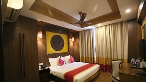 A hotel room with a bed, a desk, a chair, a ceiling fan, and curtains. - Vivin Luxury Suites (Thiruvananthapuram)