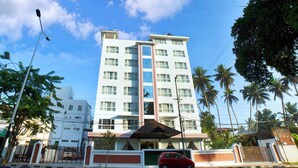 A multi-story hotel with a central entrance, surrounded by palm trees and a clear sky. - Vivin Luxury Suites (Thiruvananthapuram)