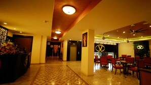 A hotel lobby with a patterned floor, a reception desk, and a dining area with red chairs and tables. - Vivin Luxury Suites (Thiruvananthapuram)