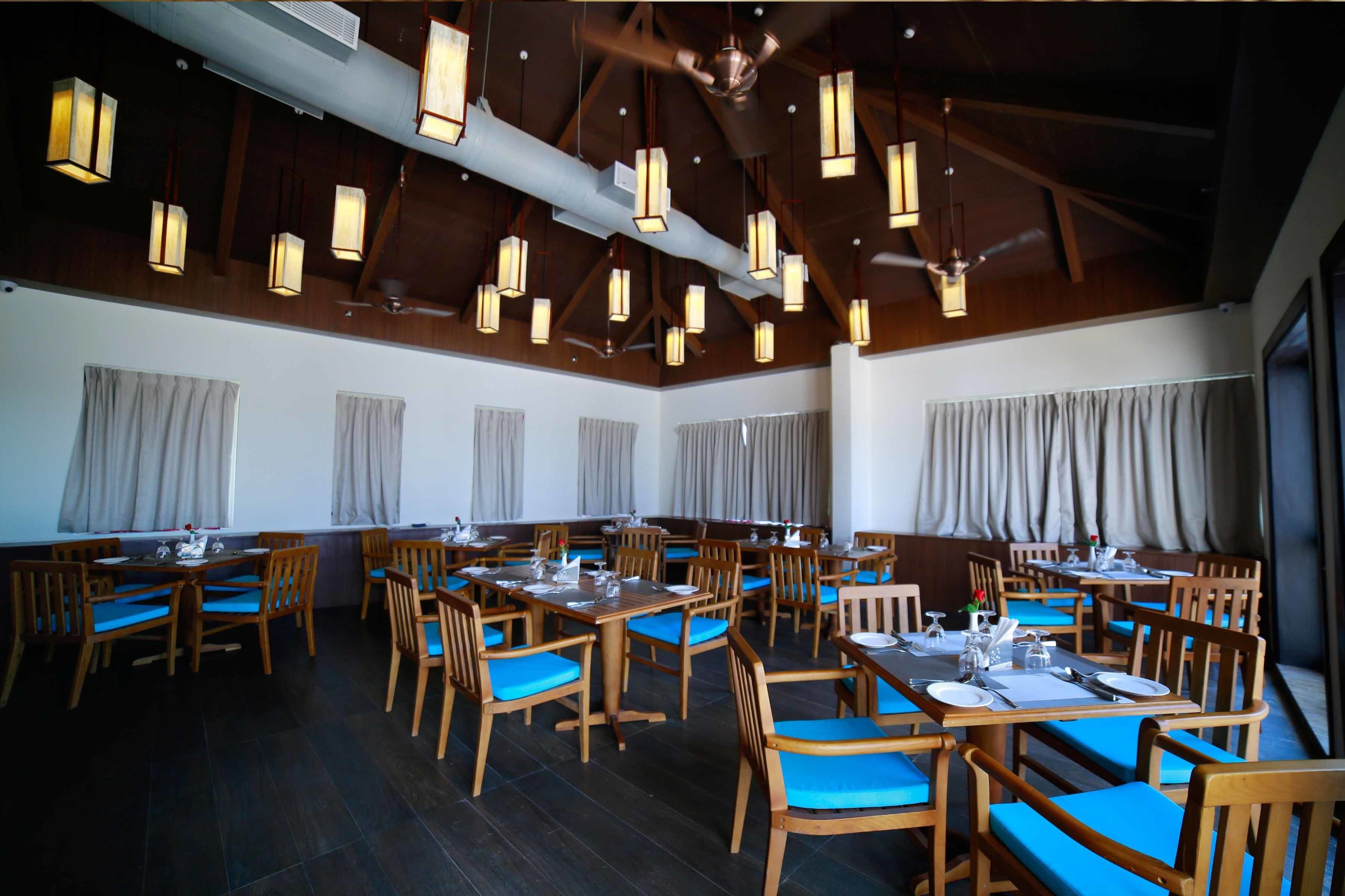 A spacious dining area with multiple tables and chairs, wooden beams on the ceiling, and hanging pendant lights.