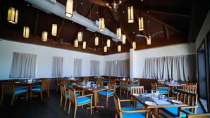 A spacious dining area with multiple tables and chairs, wooden beams on the ceiling, and hanging pendant lights. - Vivin Luxury Suites (Thiruvananthapuram)