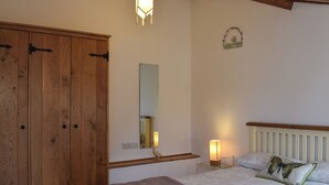 Une chambre à coucher avec une armoire en bois, une table de chevet avec une lampe, un lit avec des oreillers et un miroir fixé au mur.