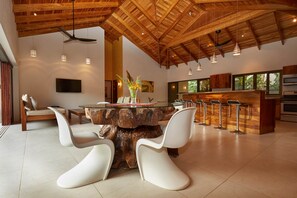A modern kitchen with a central island, bar stools, and a dining area with white chairs. - Hermandad, Short Walk to Surfing Beach | Family Retreat, Gorgeous 4 BDR home located very close to the Beach Dog Cafe  (Nosara)