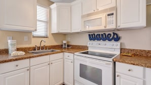A kitchen with white cabinets, a granite countertop, a microwave, and a stove. - 🌴 Gulf Winds Studio — Balcony Views & Sleep Number Comfort by the Beach (St. Pete Beach)