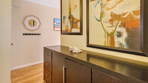 A hotel room with a wooden floor, a dark brown dresser, and two abstract paintings on the wall. - 🌴 Gulf Winds Studio — Balcony Views & Sleep Number Comfort by the Beach (St. Pete Beach)