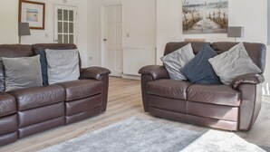 A living room with two brown leather sofas, a grey rug, and a painting of a beach scene on the wall. - 2 bedroom accommodation in Carlyon Bay, near St Austell (Carlyon Bay, near St Austell)