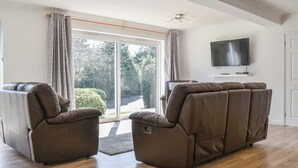 A living room with a brown sofa set, a flat-screen TV mounted on the wall, and a sliding glass door leading to a garden. - 2 bedroom accommodation in Carlyon Bay, near St Austell (Carlyon Bay, near St Austell)