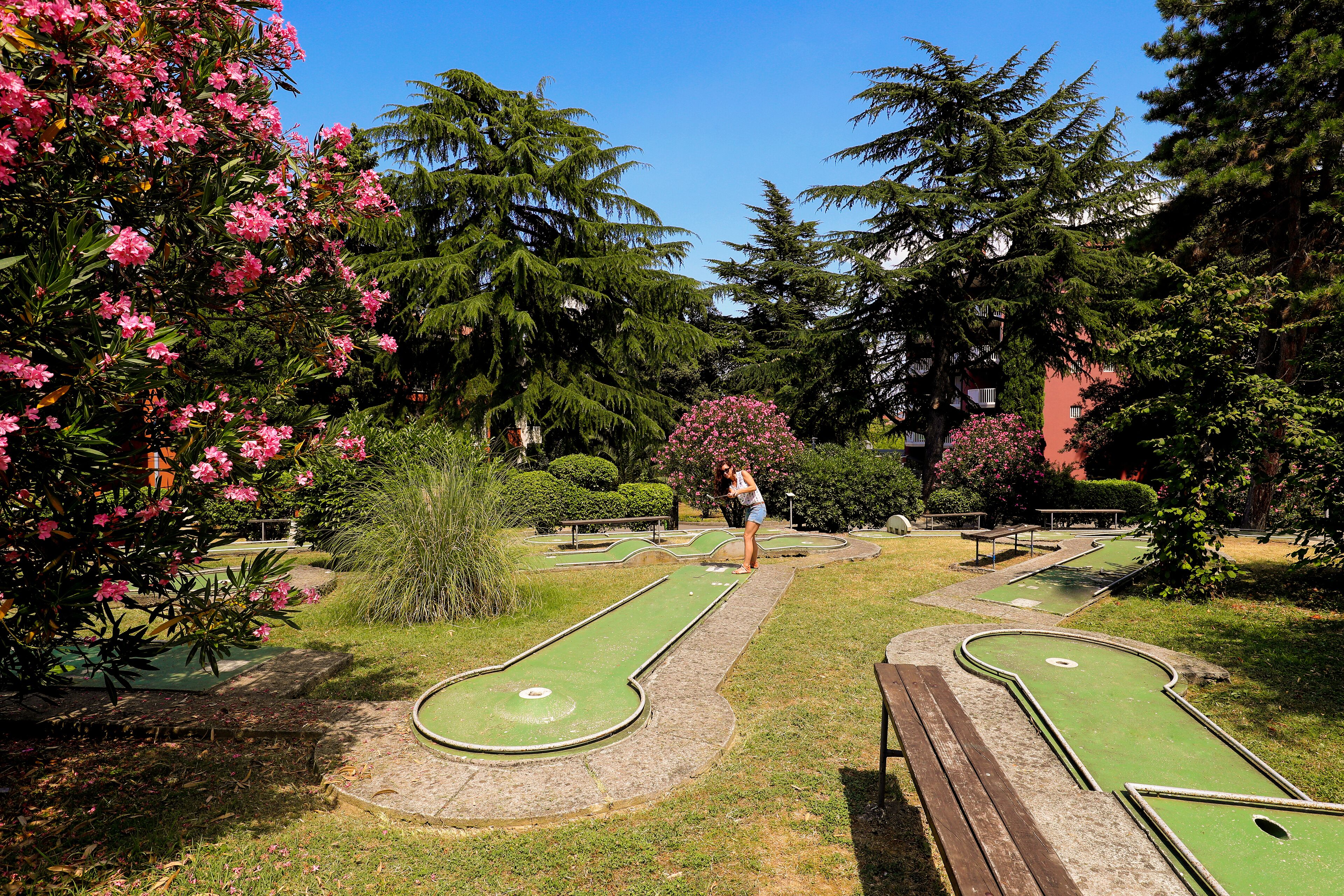 Ein Park mit zwei grünen Croquet-Rasenflächen, umgeben von Bäumen und Sträuchern.